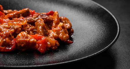 .Delicious juicy meat with hot peppers and sauce on a black ceramic plate