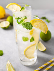 Lemonade drink with fresh lemons. Refreshing cocktail with lime, lemon, mint and ice in a tall glass on gray background close up.