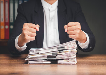 Businessman fists over a stack of documents while sitting at the table in the office