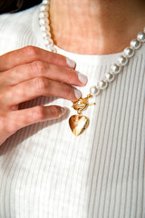 hand holding a necklace with golden heart and pearls