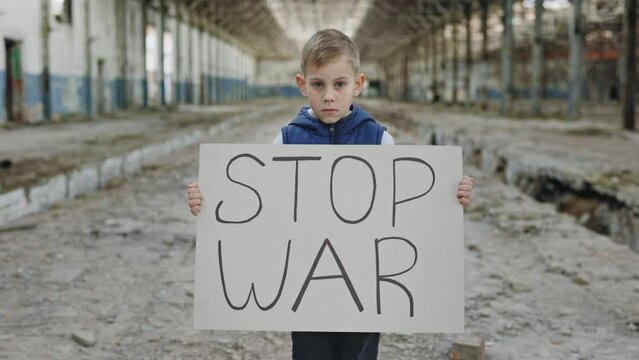 Portrait serious blond boy protesting war holding banner with inscription stop war. Call to stop war, child against war, crisis in Ukraine