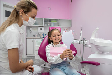 little female patient in the dental chair looks at her teeth after their treatment.