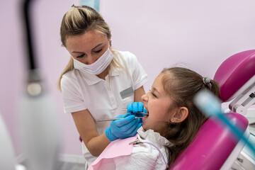  little patient grimaces during an examination of the oral cavity by a female dentist.