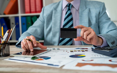 Close-up of human hand of man holding credit card while working on laptop and documents.