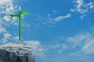 2023 and 2022 direction sign plate with green pencil on rock mountain over blue sky with white clouds, Business strategy planning concept, Happy new year 2023 calendar cover
