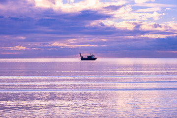 A cold day in Troon Scotland as the sun starts to go down behind the horizon and a loan fishing boat in the Bay