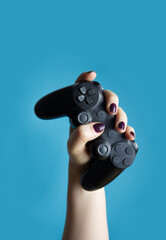 A female hand holds a controller from a video console on a blue background close-up © Natalia Maliseva