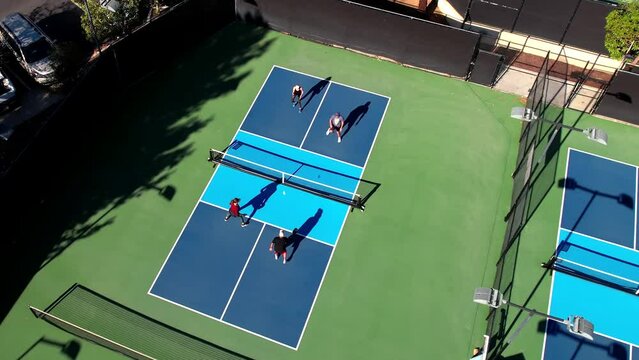 Pickleball match on blue outside court, foursome playing the sport, drone rising over players