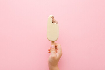 Baby girl hand holding chocolate ice cream with white vanilla glaze on light pink table background....