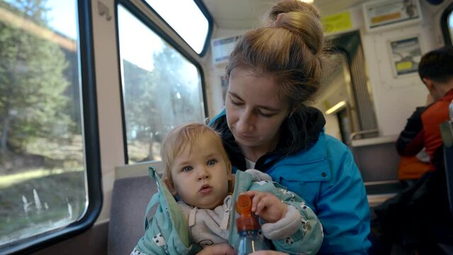 Loving mother kisses little daughter sitting near window with bright back sunlight. Woman and baby girl enjoy traveling by train closeup slow motion