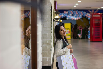 Young asian woman smiling and brings shopping bags spending time in shopping mall