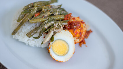 A plate of rice with egg balado and long bean sauce, chili sauce filled with eggs, anchovies and tofu. Served in a bowl on a gray background. Selected focus.