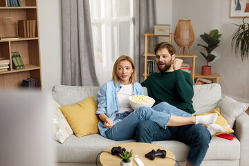 Laughing Couple Watching TV At Home. Loving People Resting On Sofa And Eating Popcorn At Cozy Home Morning. Leisure Concept 