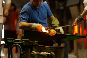 A glass blower is working on the manufacture of glass vases and glasses.