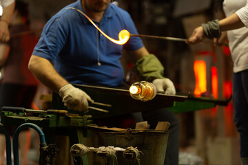 A glass blower is working on the manufacture of glass vases and glasses.