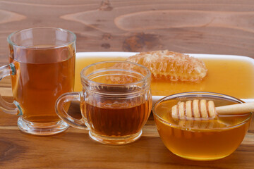 a bowl of honey with honey dipper, glass cup of tea, and honeycomb on wooden table