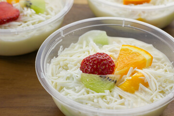 selective focus creamy fruit salad served in plastic bowl on wooden background