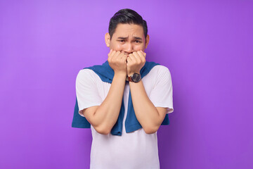 Scared young Asian man wearing white t-shirt Gnawing nails and looking serious on the camera isolated over purple background. people lifestyle concept