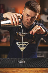 Bartender carefully filters alcoholic cocktail
