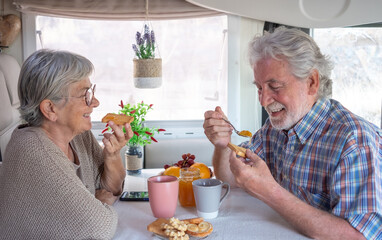 Beautiful caucasian senior couple in travel vacation leisure inside a camper van dinette enjoying breakfast together. Happy retired and free lifestyle