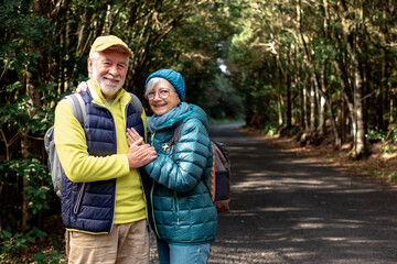 Front view of smiling senior couple enjoying freedom in outdoors walking in a mountain forest. Elderly cheerful couple traveling together in a park