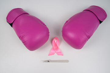 Pink boxing gloves, a surgical scalpel and a pink ribbon on a white background. The concept of...