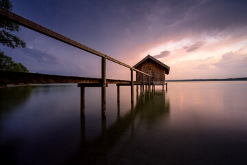 Fototapeta na wymiar Bootshaus mit Steg am See mit farbigem Himmel.