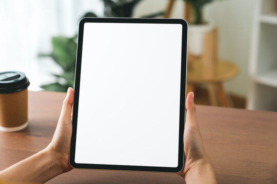 Hands holding digital tablet with mockup of blank screen on sofa in living room.
