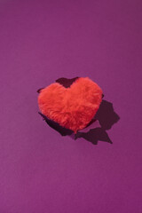Pink fluffy plush heart on torn purple background. Minimal retro love or Valentine's concept.
