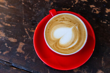 A red cup of coffee cappuccino with latte art on wooden background. Coffee house