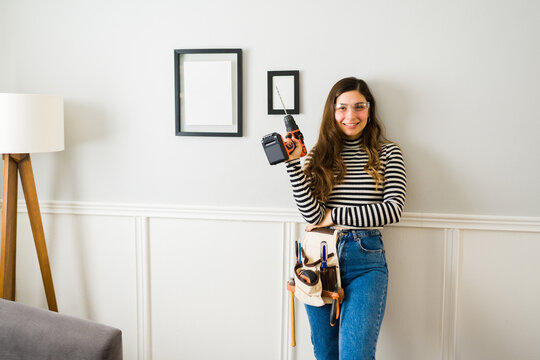 Beautiful woman ready to hang pictures on the wall with a drill