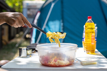 Crop man adding pasta in bowl during camping