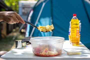 Crop man adding pasta in bowl during camping