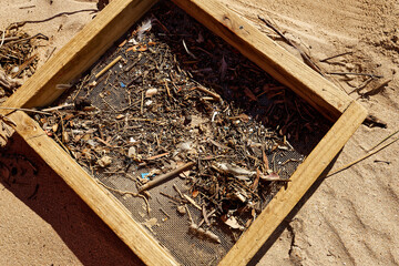 A sieve with a wooden frame used by workers to remove small plastic particles from the beaches of...