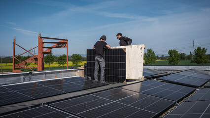 Male team engineers installing stand-alone solar photovoltaic panel system. Electricians mounting blue solar module on roof of modern house. Alternative energy concept