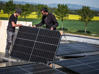Male team engineers installing stand-alone solar photovoltaic panel system. Electricians mounting blue solar module on roof of modern house. Alternative energy concept