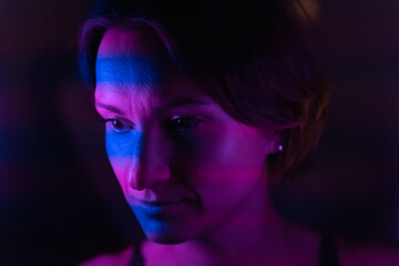 Fototapeta premium Stripes of blue and purple neon light up the face of a young dark-haired woman