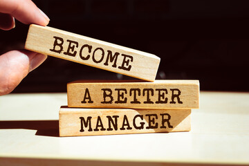Closeup on businessman holding a wooden blocks with text BECOME A BETTER MANAGER, business concept