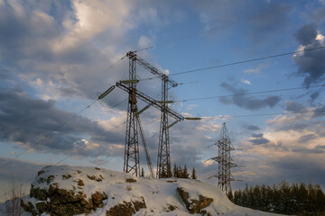 Mast of a high-voltage power line against the cloudy sky.