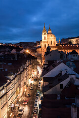 Fototapeta na wymiar Beleuchtete Straße zur blauen Stunde mit alten Häusern und Kirche in Prag.