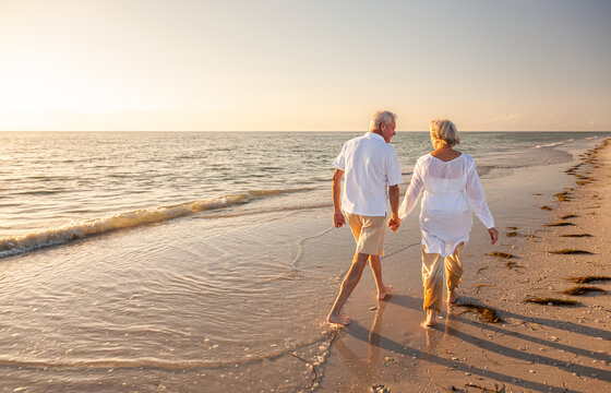 Happy Senior Old Retired Couple Walking Holding Hands on Beach at Sunset