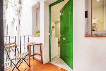Small terrace with a folding wooden table with matching chair next to a green entrance door