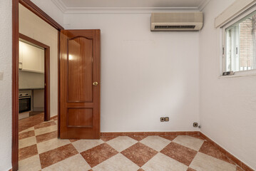 Empty room with air conditioning installation, checkered stoneware floors and varnished sapele wood door