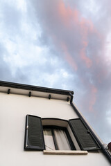 Detached house with window with green shutters and a sunset sky with blues and golds