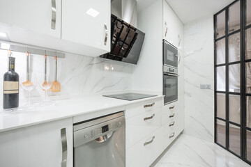 Kitchen with white furniture and stainless steel and glass appliances, many drawers and a French-style glass wall