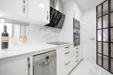 Kitchen with white furniture and stainless steel and glass appliances, many drawers and a...