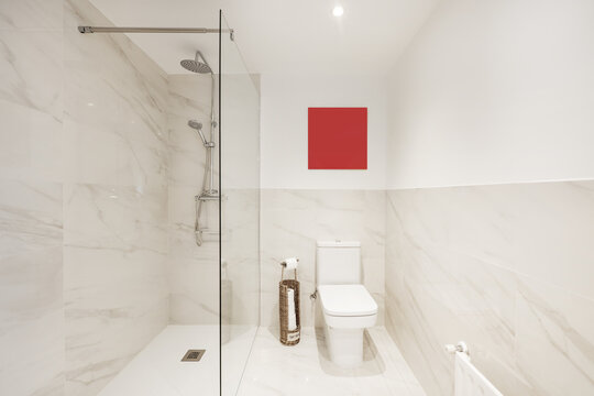Bathroom with white porcelain toilet, mirror with matching frame, marble tiles and glass-enclosed shower stall