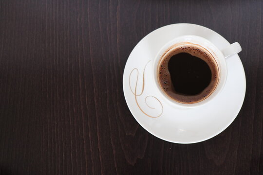 A photo of a white mug with coffee in it, shot on a wooden background.