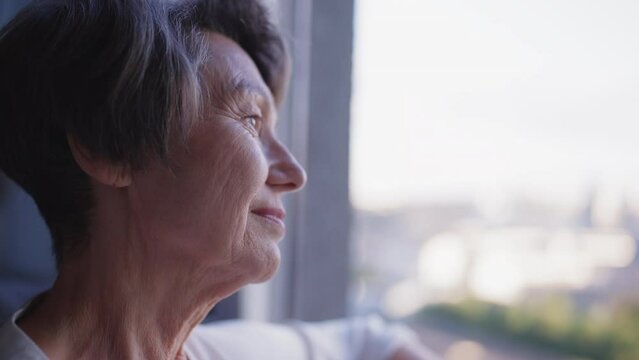 Closeup of beautiful senior woman looking out window and smiling, good memories