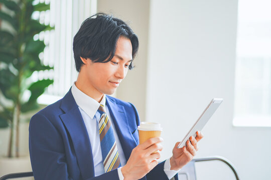 休憩中にタブレットを見ながらコーヒーを飲むビジネスマン